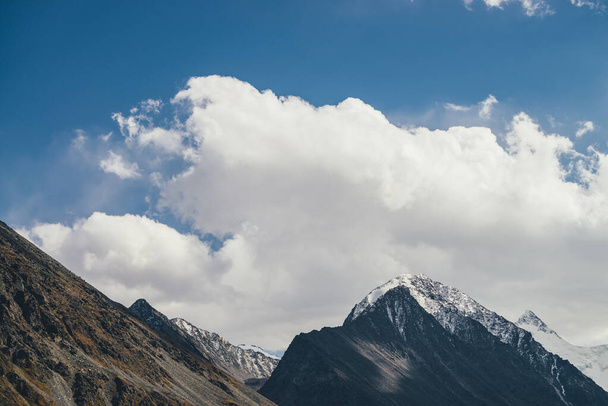 Paisagem alpina atmosférica com silhueta de montanha alta com neve no topo de pico sob o céu azul nublado. Cenário montanhoso dramático com belo pico pontiagudo coberto de neve e alta parede de montanha nevada - Foto, Imagem