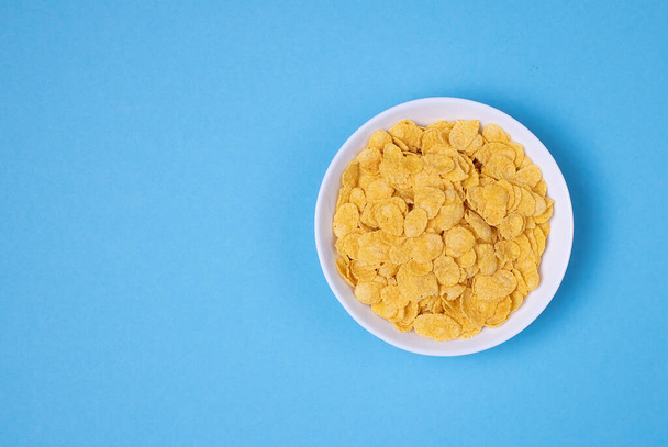 Cornflakes in weißer Schale auf blauem Hintergrund für Getreide und gesunde Ernährung. Ansicht von oben. Kopieren, leerer Raum für Text - Foto, Bild