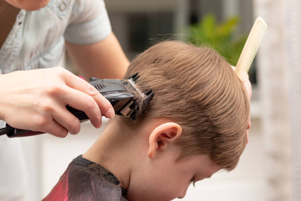 Nuori äiti kampaaja leikkaa poikansa kotona hiustenleikkurilla karanteenin aikana. valikoiva kohdentaminen. muotokuva - Valokuva, kuva