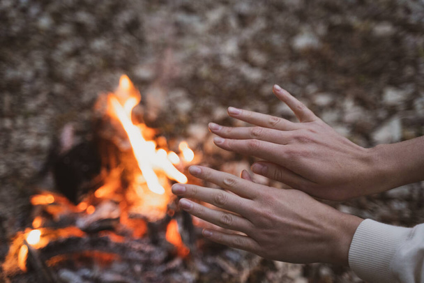 A woman warms her hands over a fire in a campsite. Journey to the forest - Foto, Bild
