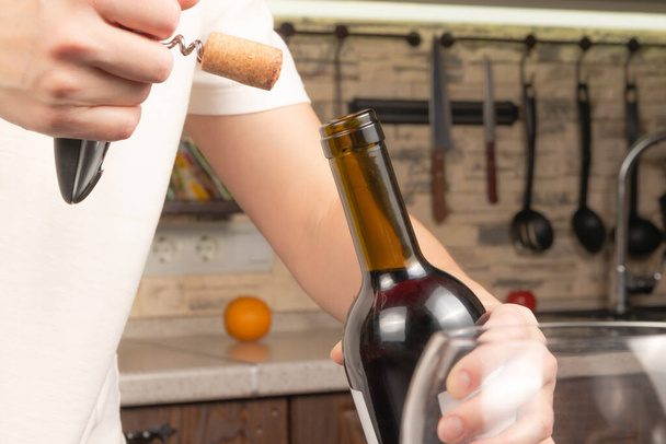 manos femeninas abren una botella de vino tinto seco con un sacacorchos en el fondo de la cocina. enfoque selectivo. primer plano - Foto, Imagen