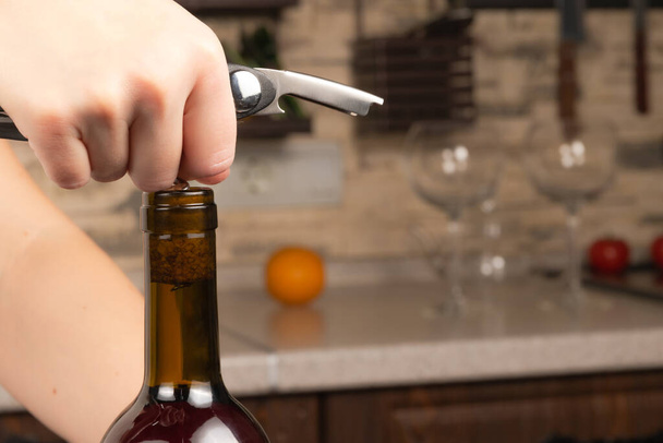 manos femeninas abren una botella de vino tinto seco con un sacacorchos en el fondo de la cocina. enfoque selectivo. primer plano - Foto, imagen