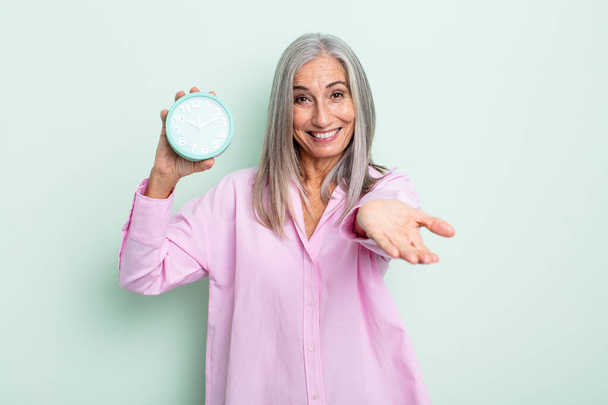 middle age gray hair woman smiling happily with friendly and  offering and showing a concept. alarm clock concept - Foto, Imagen