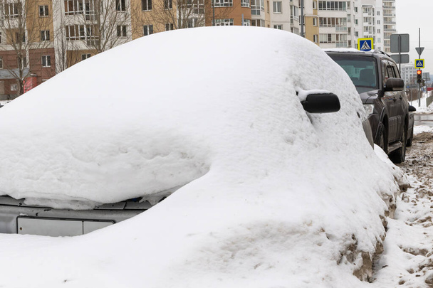 staré opuštěné rozbité auto zaparkované u silnice pod velkou vrstvou sněhu v chladném zimním dni - Fotografie, Obrázek