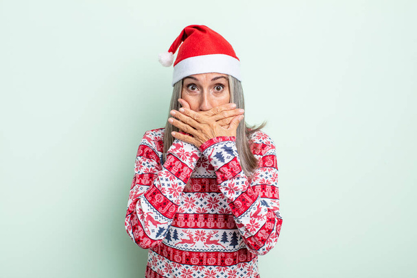 šedovlasá žena středního věku zakrývající ústa šokovanýma rukama. vánoční koncept - Fotografie, Obrázek
