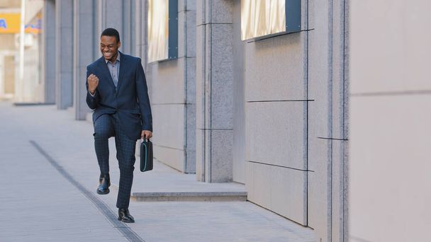 Happy funny young businessman dancing alone outdoors celebrating Friday, work achievement professional success, reward or promotion, excited Afro-American male employee enjoy victory dance on street - Photo, Image