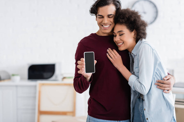 happy man holding smartphone with blank screen near smiling african american girlfriend   - Photo, Image