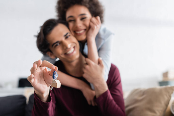 happy man holding key from new home while hugging with smiling african american girlfriend   - Photo, Image