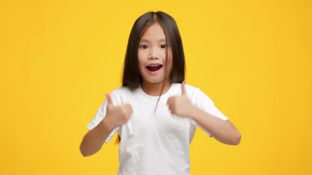 Kis ázsiai lány Gesturing hüvelykujj fel pózol át sárga háttér - Felvétel, videó