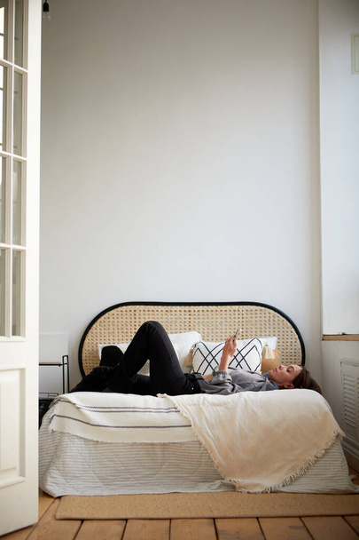 Vrouw liggend op bed en browsen smartphone - Foto, afbeelding