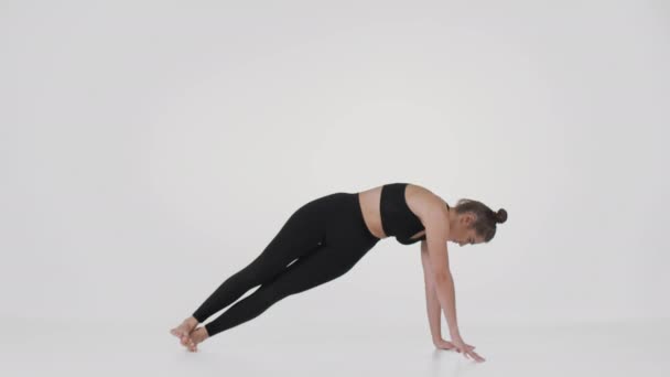 Yoga para principiantes. Joven mujer flexible apoyada en su mano y estirándose, practicando sobre fondo blanco - Metraje, vídeo