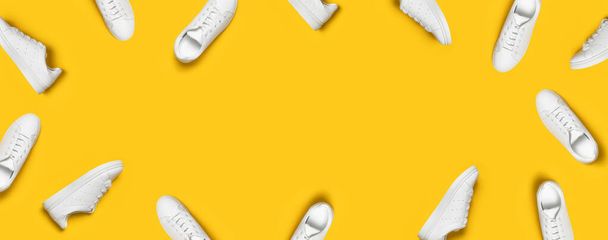 Weiße Damen-Lederturnschuhe auf gelbem Hintergrund mit flachem Lagemuster. Stylische Jugendturnschuhe, Sportschuhe, echte Lederschuhe. Minimalistische Schuhgeschäft Werbung Mode Stil Schuh Hintergrund. - Foto, Bild