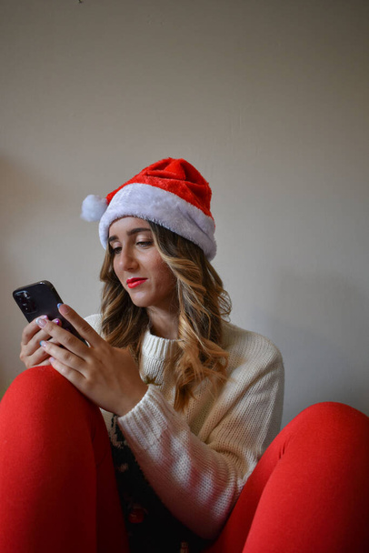 A happy female in a Santa hat browsing her phone - Fotoğraf, Görsel