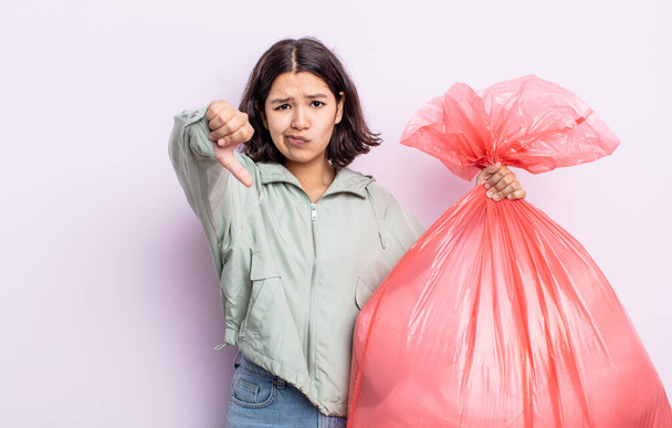 pretty young woman feeling cross,showing thumbs down. trash bag concept - Photo, image