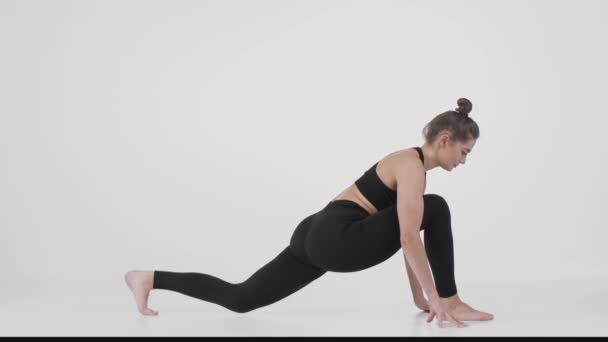 Estilo de vida deportivo. Mujer joven practicando el entrenamiento de pilates, estirando la espalda y de pie en posición de perro descendente - Imágenes, Vídeo
