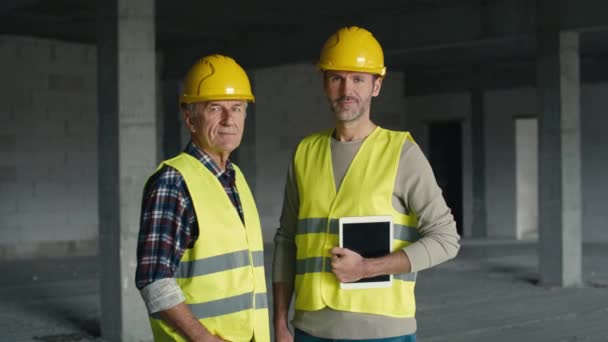 Kahden valkoihoisen insinöörin muotokuva, joilla on digitaalinen tabletti rakennustyömaalla. Laukaus punaisella heliumkameralla 8K   - Materiaali, video