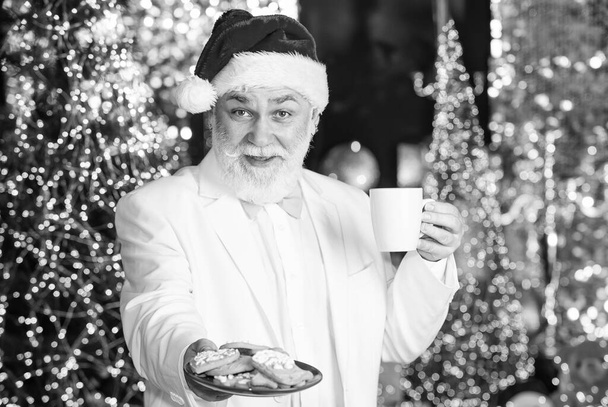Santa Claus near christmas tree. Merry christmas. Bearded senior man Santa Claus. Santa Claus relaxing. Winter vacation. Elderly grandpa at home. Traditions concept. Coffee break. Sweets and treats - 写真・画像