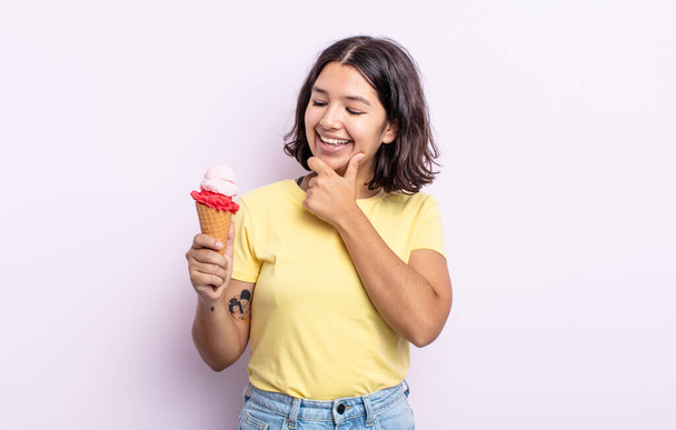 mujer joven y bonita sonriendo con una expresión feliz y segura con la mano en la barbilla. concepto de helado - Foto, imagen