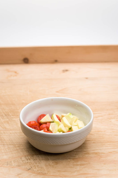 white stoneware bowl with datterini tomatoes and zucchini chunks on a worn wooden background - Foto, imagen