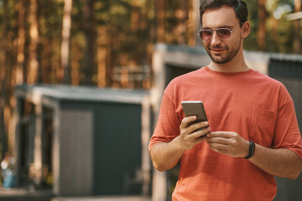 Smiling man looking into smartphone outdoors - Fotografie, Obrázek