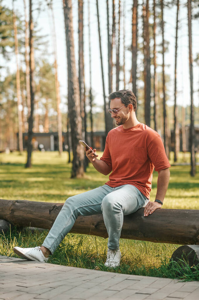 Smiling man with smartphone sitting in nature - Fotoğraf, Görsel