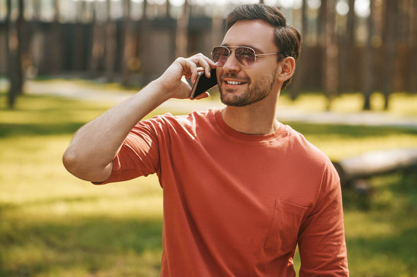 Cheerful man with smartphone near ear outdoors - Foto, afbeelding