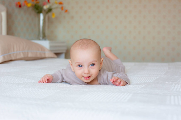 baby boy is lying on the bed in the bedroom on his stomach - Фото, изображение