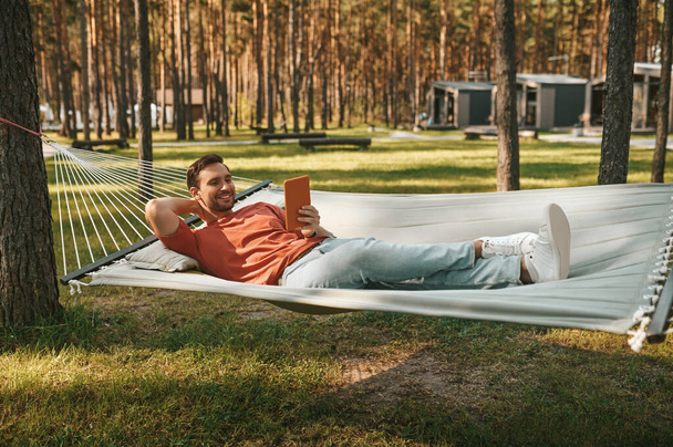 Attractive man looking into tablet relaxing on hammock - Fotó, kép
