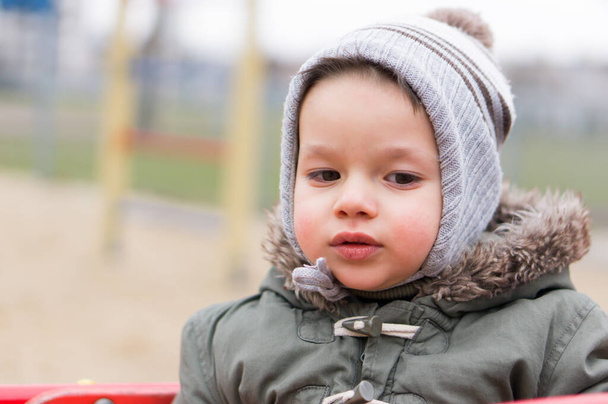 A closeup shot of a two years old caucasian child sitting in a playground roundabout on a cold day. - Foto, afbeelding