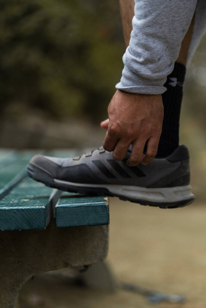 A vertical shot of a male tying his shoe on a bench outdoors - Фото, зображення
