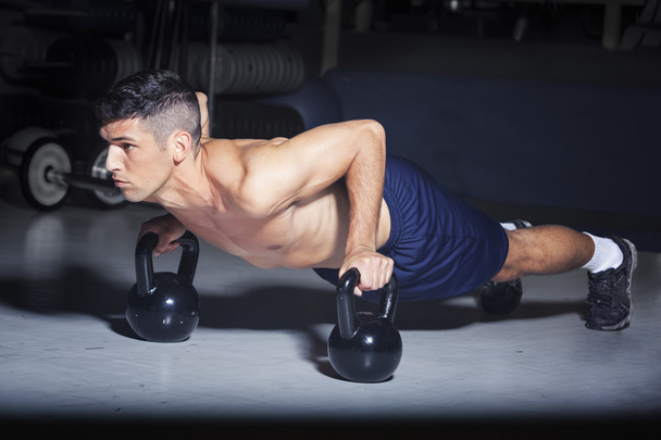 Man doing push-ups with kettlebells in gym - 写真・画像