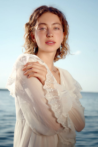 A vertical shot of an attractive Russian female in a beautiful white dress posing by the lake - Foto, immagini