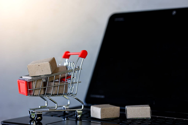 Winkelen online en levering concepten. Product pakketdozen in winkelwagen met laptop computer op houten tafel. - Foto, afbeelding