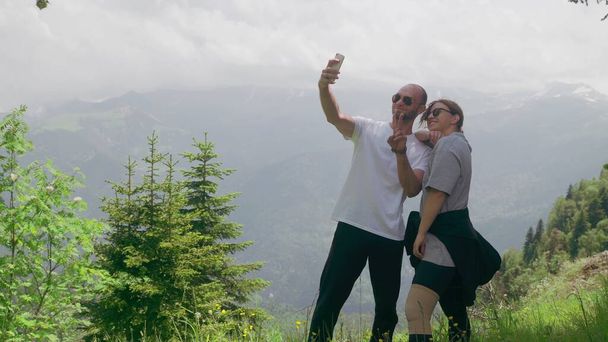 Un jeune homme et une jeune fille se tiennent dans une région montagneuse et prennent des selfies sur leur téléphone. Voyages - Photo, image