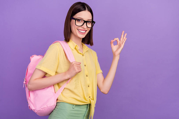 Profile side photo of young lady backpack study show okey symbol approve good isolated over violet color background - Foto, afbeelding