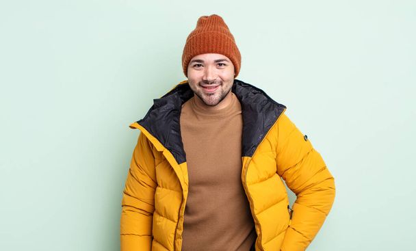 young handsome man smiling happily with a hand on hip and confident. cold weather concept - Fotó, kép