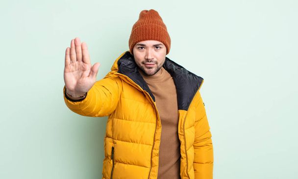 young handsome man looking serious showing open palm making stop gesture. cold weather concept - Foto, Imagen