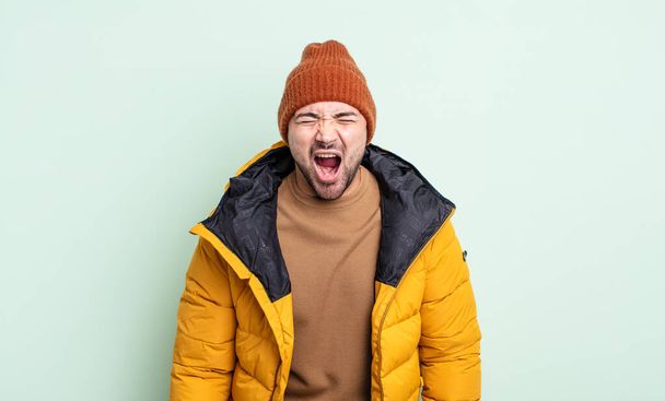 young handsome man shouting aggressively, looking very angry. cold weather concept - Fotó, kép