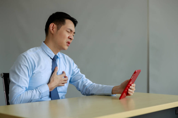 азіатський бізнесмен сидить відчуваючи біль груди в офісі під час відеодзвінка
 - Фото, зображення