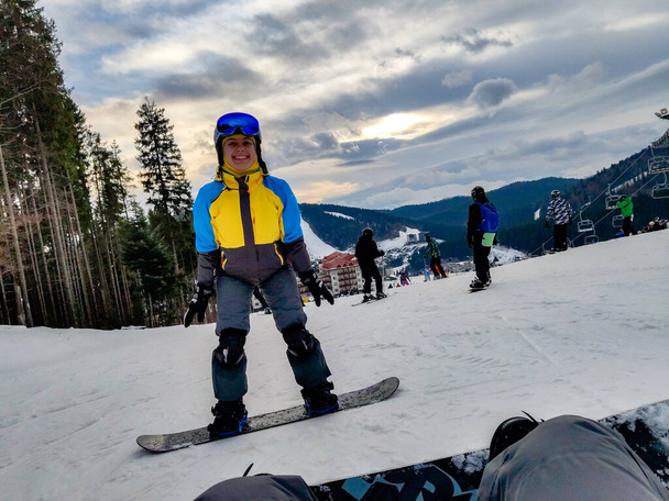 hombre sentado en la colina nevada con snowboard mujer feliz en frente estación de esquí de invierno - Foto, Imagen