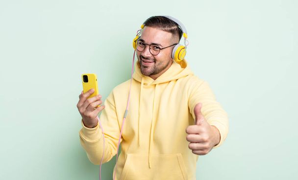 young handsome man feeling proud,smiling positively with thumbs up. headphones and smartphone concept - 写真・画像