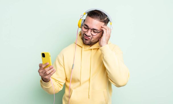 young handsome man feeling bored, frustrated and sleepy after a tiresome. headphones and smartphone concept - Photo, Image