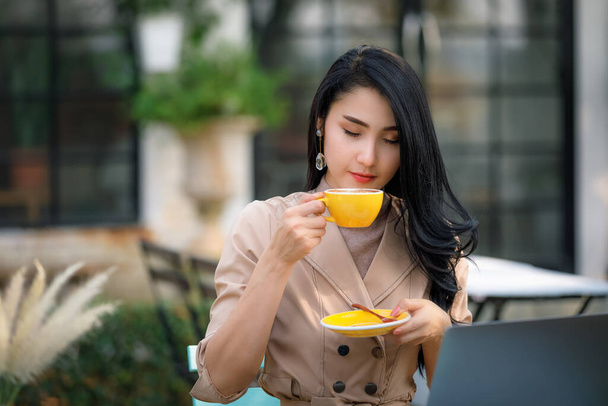 junge asiatische Geschäftsfrauen und Freiberuflerinnen sitzen auf einem Holztisch im Garten und trinken entspannt Kaffee   - Foto, Bild
