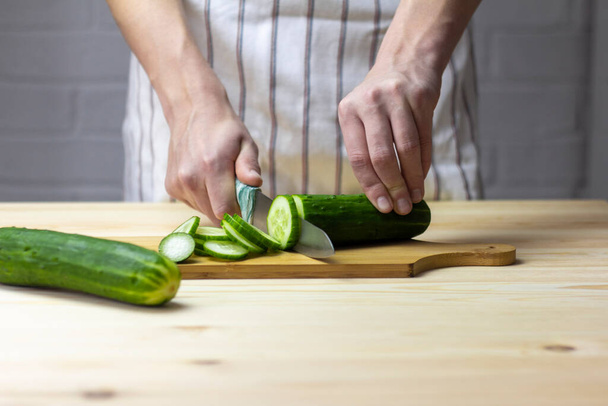 Un giovane taglia con cura un cetriolo con un coltello su un tagliere - Foto, immagini