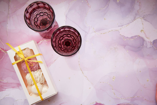 Festliche Weingläser und zartes rosa und weißes Eibisch mit Dekoration flüssiger Kunst. Weibliches Kartenkonzept. Gemütliche Winterwochenenden mit Kaffee und Süßigkeiten. Hausgemachte Köstlichkeiten. Ansicht von oben. Hochwertiges Foto - Foto, Bild