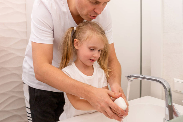 Mann wäscht Mädchen die Hände mit einem Stück weißer Seife im Badezimmer. Baby hygiene - Foto, Bild