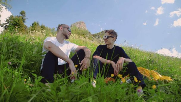 Siyah gözlüklü iki genç bir yamaçta oturuyor ve dağlık bir alanda sohbet ediyorlar. Turizm ve seyahat - Fotoğraf, Görsel