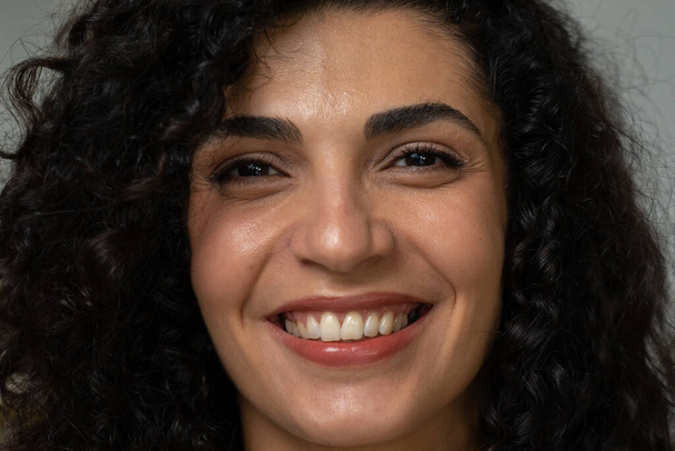 Close-up of the face of a cheerful young mixed-race woman with curly hair in a white shirt, posing and looking at the camera - Fotografie, Obrázek