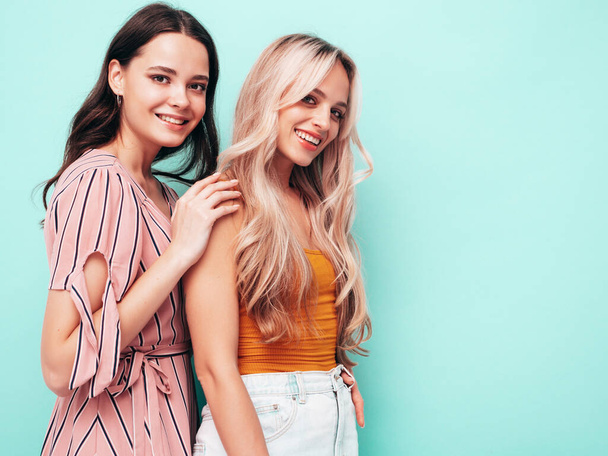 Two young beautiful smiling brunette hipster female in trendy summer clothes. Sexy carefree women posing near blue wall. Positive models having fun. Cheerful and happy - Zdjęcie, obraz