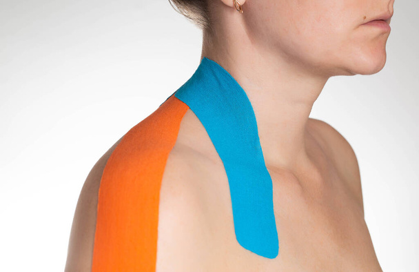 Fixation of muscles and ligaments on the girls shoulder with blue and orange kinesiological tape, close-up. Taping in sports - Zdjęcie, obraz